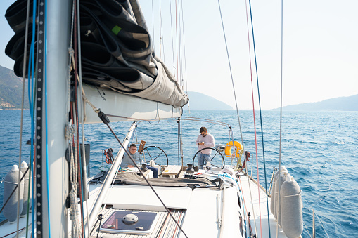 Businessman, owner with mobile phone at steering wheel in voyage sail on sport sea luxury yacht. Yachting summer vacation cruise. Sailing on ocean ship boat travel. Enjoy trip on sailboat front deck.