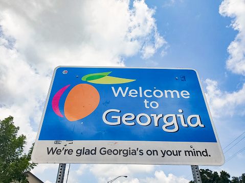 This is a photograph taken of the Welcome to Georgia sign marking the state line at the border on a sunny day with clouds during the summer of 2020