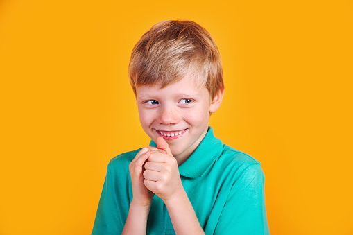 Closeup portrait of sneaky sly scheming kid boy on yellow studio background