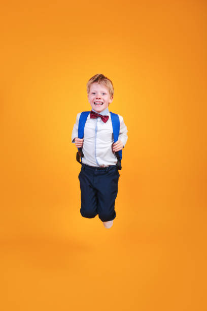 istock Funny school boy with a backpack jumping on yellow studio background 1485506630