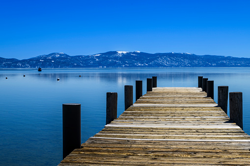 Wide winter view of Lake Tahoe and lakeside pier, with snow covered mountains in background.\n\nTaken from Northshore of Lake Tahoe, California, USA  looking South.
