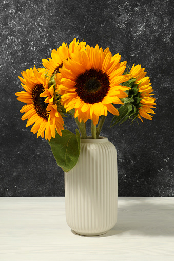 Vase with beautiful sunflowers on white table against black background