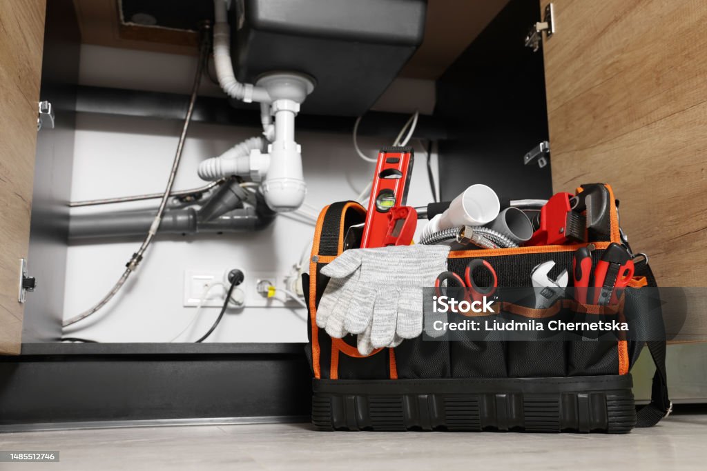 Plumber's tool bag on floor under kitchen sink Water Pipe Stock Photo