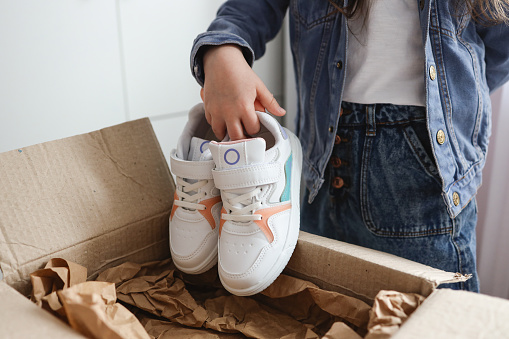 A little girl unpacks the parcel, sneakers in her hands.