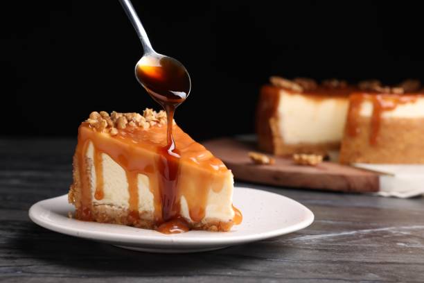 istock Pouring caramel sauce onto delicious piece of cheesecake with walnuts on black marble table, space for text 1485520249