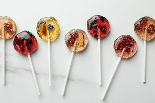 Sweet colorful lollipops with berries on white marble table, flat lay
