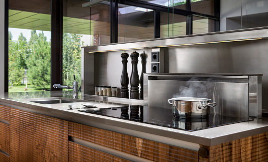 Steel pot with boiling and steaming food in modern wood and stainless steel kitchen. Cooking.