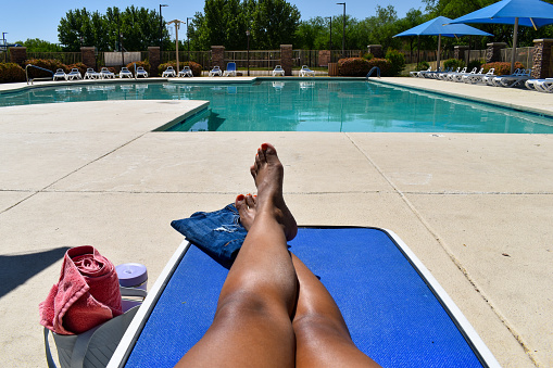 A beautiful African-American woman hanging out poolside. Soaking up the sun while doing relaxing activities like reading, journaling, taking selfies, and applying sunscreen.