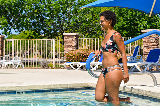 A beautiful African-American woman hanging out at the pool. Dipping her feet in. Getting in the water. And taking a relaxing swim.