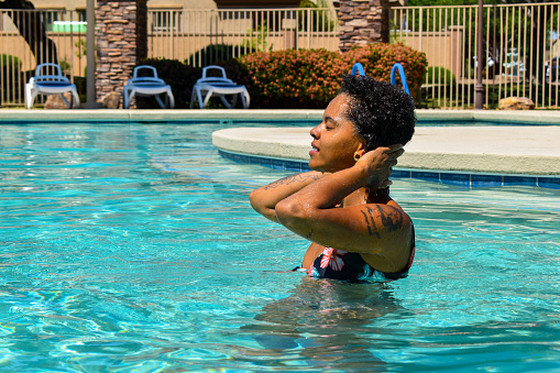 A beautiful African-American woman hanging out at the pool. Dipping her feet in. Getting in the water. And taking a relaxing swim.