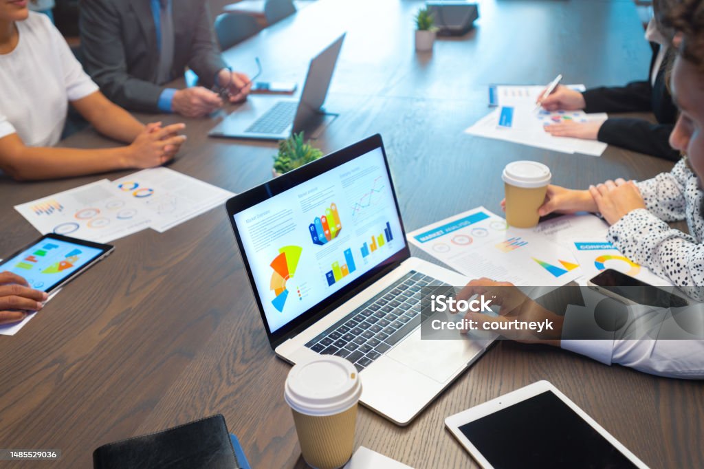 Group of business people working at a conference table. Group of business people working at a conference table. There is paperwork a laptop and technology with financial graphs, charts and figures. Chart Stock Photo