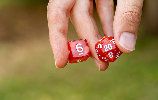 Man holding two different simple red classic RPG game dice, objects held in hand detail, closeup Role playing board games, live action roleplay LARP symbol abstract concept, copy space, one person