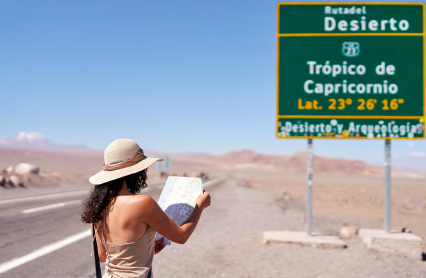 rear view tourist woman holding and reading a map on the road in front of a tropico de capricorn sign in the desert of atacama rear view tourist woman holding and reading a map on the road in front of a tropico de capricorn sign in the desert of atacama tropic of capricorn stock pictures, royalty-free photos & images