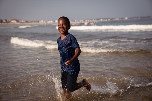 Black child plays on the beach and in the water off the coast of Maine on a summer afternoon.  The boy is joyous and enjoys  the warm water.