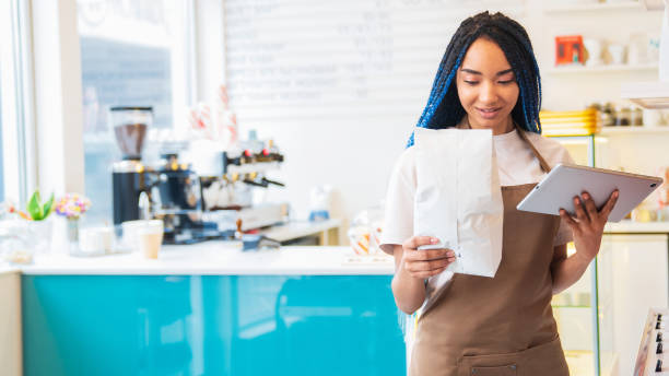 istock Pretty young woman holding coffee package while using digital tablet in coffee shop 1485536139