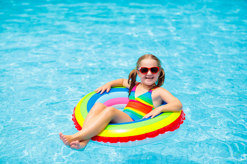 Child in swimming pool floating on toy ring. Kids swim. Colorful rainbow float for young kids. Little girl having fun on family summer vacation in tropical resort. Beach and water toys. Sun protection.