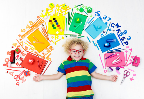 Little boy with school supplies, books, drawing and painting tools and materials. Happy back to school student. Art and crafts for kids. Child learning rainbow colors, alphabet letters and numbers.