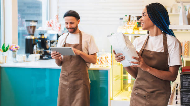 istock Lady holding paper package with coffee beans, man using digital tablet in coffee shop 1485539701