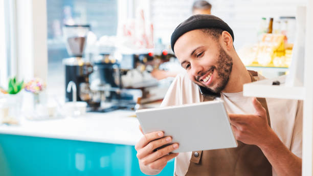 istock Happy male coffee shop worker using phone and tablet, taking orders online 1485539757