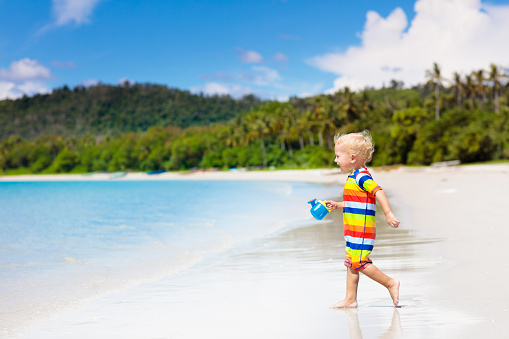 Child playing on tropical beach. Little boy digging sand at sea shore. Family summer vacation. Kids play with water and sand toys. Ocean and island fun. Travel with young children. Asia holiday.
