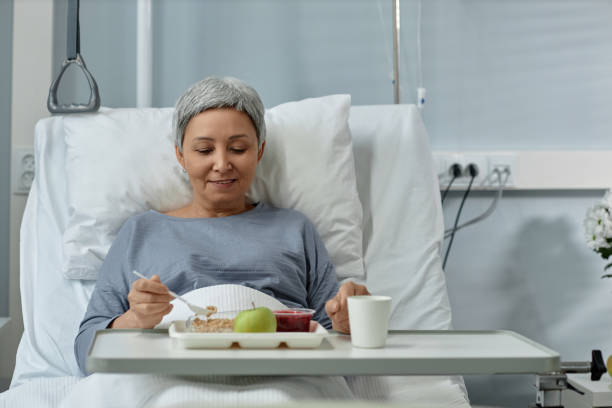 Mature woman having lunch in ward Mature woman sitting on bed and eating healthy food during lunch in ward sick woman hospital bed stock pictures, royalty-free photos & images