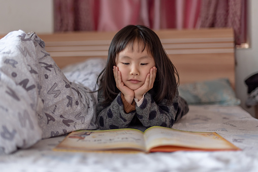 An Asian girl is reading in bed at home