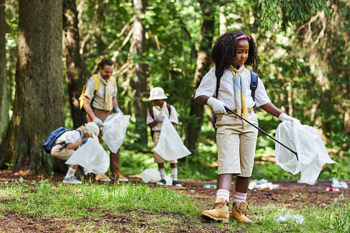 Full length portrait of cute black girl as girl scout helping clean forest and holding trash bag, copy space