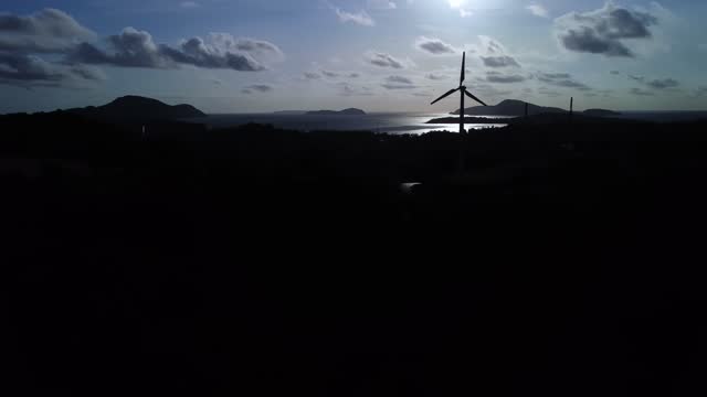 Silhouette of electric station with wind mill located on the shore of ocean filmed by drone