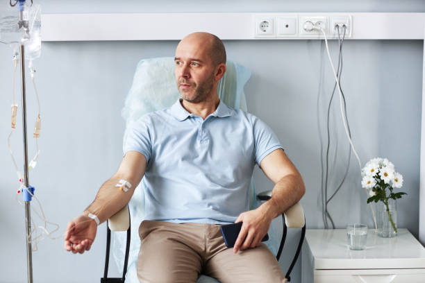 adult man sitting in chair with iv drip during treatment session in clinic - chemotherapy drug imagens e fotografias de stock