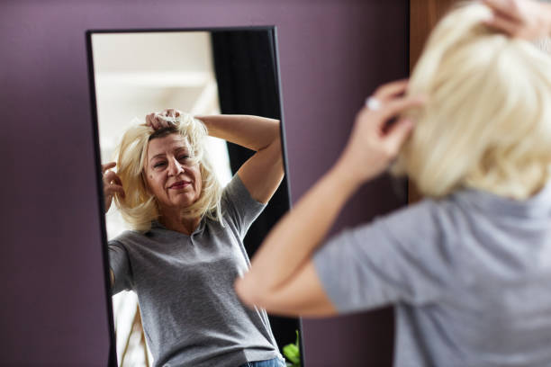 istock Mature bald woman putting on wig looking in mirror 1485546694