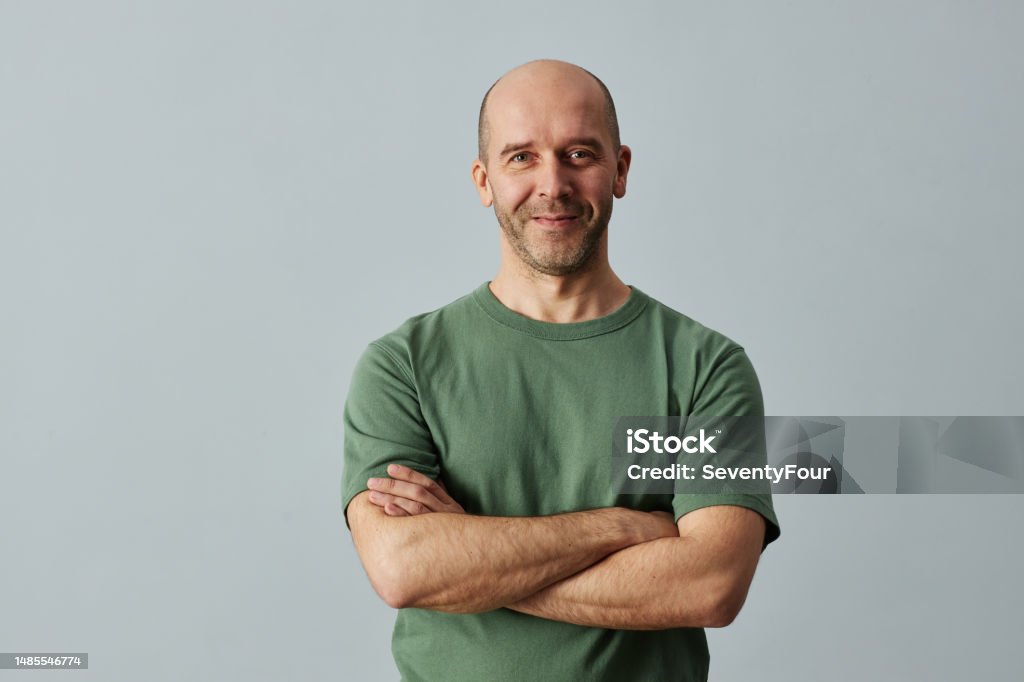 Bald man smiling at camera standing with arms crossed Minimal waist up portrait of mature bald man smiling at camera while standing confidently with arms crossed, copy space Men Stock Photo