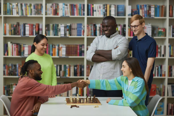 istock Two chess players shaking hands over table with group of people watching match 1485549090
