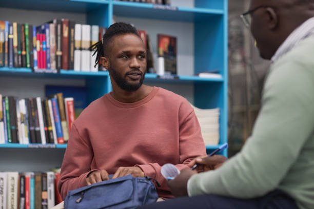 Black young man talking to therapist or guidance counsellor in college library
