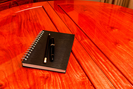 Stationary on a rosewood table ready for a meeting. Placed on the table are a noteboook, pen and pencil. No people. Copy space.