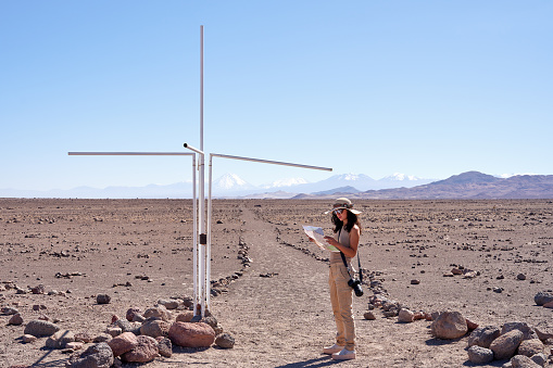 tourist woman holding and looking a map at milestone that marks the passage of the parallel of the Tropic of Capricorn through San Pedro de Atacama