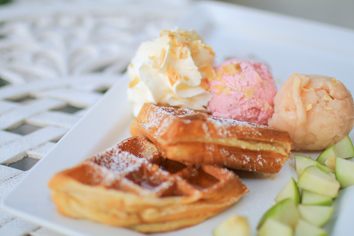Hand pouring maple syrup on waffle and ice cream with apple on white table in garden. Tea time situation in bright mood background.  Healthy food concept