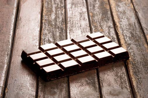 Front view of dark chocolate tablet over rustic wood table in the kitchen to be used to make a delicious cake.