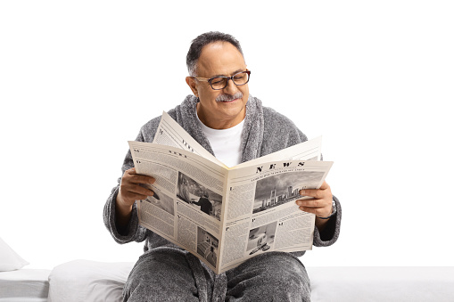 Mature man in a robe relaxing with a newspaper isolated on white background