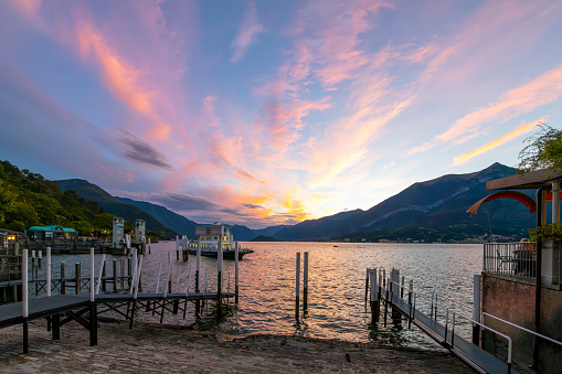 A ferry pulls away from the Lungolago Europa promenade as the sun sets and the sky turns pink over the mountains and Lake Como, in Bellagio, Italy.