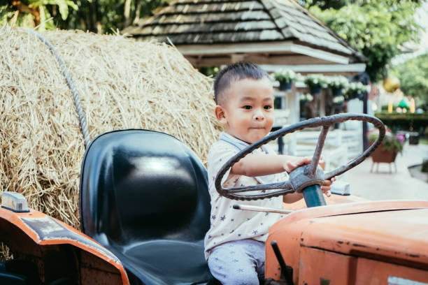 Shot of adorable little Asian baby boy holding steering wheel old tractor on the farm with copy space for your text.