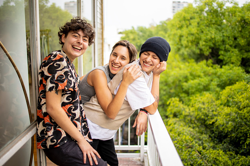 Three young Latin women standing on the balcony and laughing . They are looking at the camera