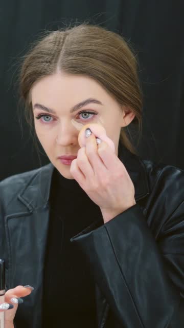 Woman applying concealer to under-eye circles in a backstage
