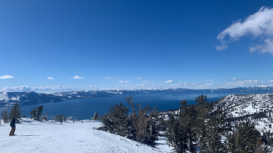 Skier above beautiful alpine lake - Lake Tahoe - in winter with a fresh snowfall covering the trees and distant mountains of the Sierra