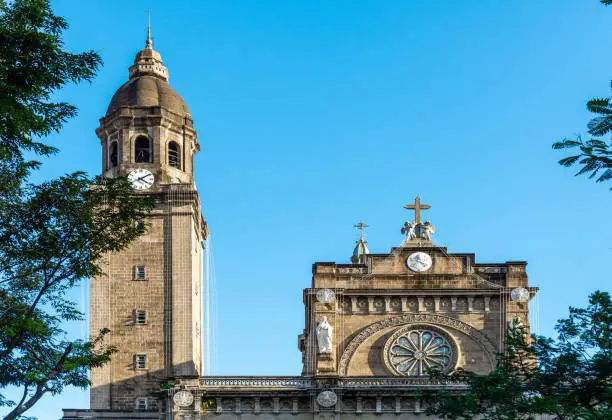 The Minor Basilica and Metropolitan Cathedral of the Immaculate Conception,front view of bell tower and roof,inside the historic walled city,within today's modern city of Manila.Blue,sunny sky.