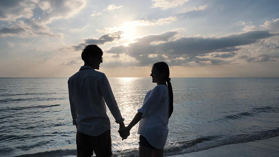Happy Romantic Young couple holding hands Enjoying Beautiful Sunset on the Beach. Travel Vacation