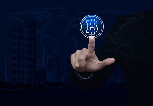 Businessman pressing bitcoin icon over world map, modern city tower and skyscraper, Choosing bitcoin concept, Elements of this image furnished by NASA