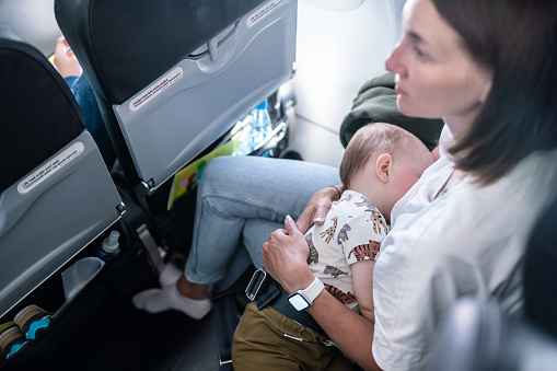 Cute little boy sleeping in mother's hands during the flight on commercial airplane