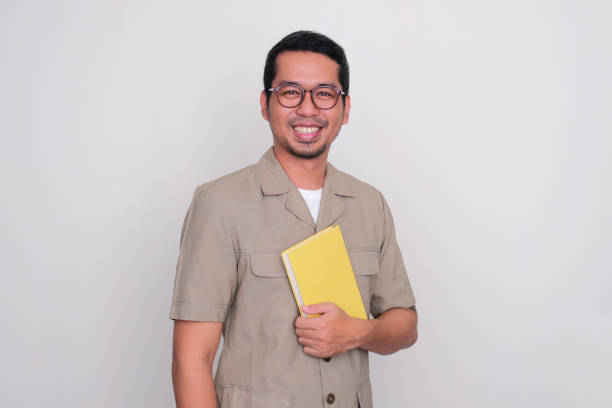 istock Indonesian school teacher standing proud while holding a book in his chest 1485642553
