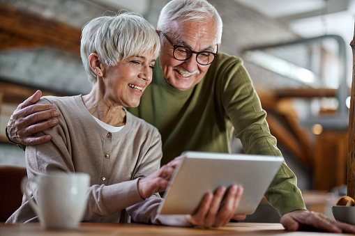 Happy senior couple surfing the Internet on touchpad at home. Focus is on woman.