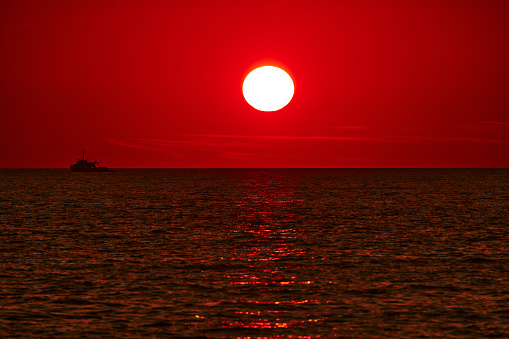 Big sunrise sunset over ocean sea horizon with silhouette of a fishing boat.
